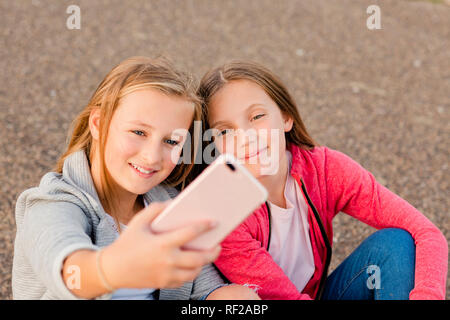 Portrait of two smiling girls taking selfie with smartphone Stock Photo