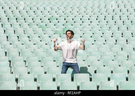 A young handsome man stands in an empty stadium alone and celebrates a win and shows a feeling of success Stock Photo