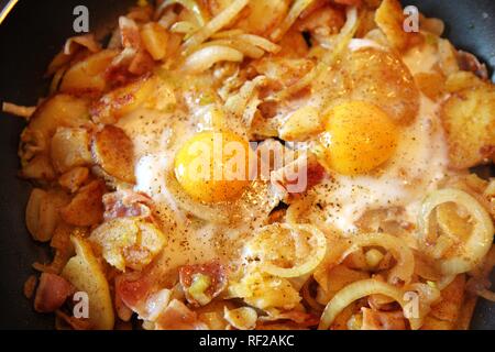 Omelette prepared in a frying pan, fried potatoes, onions, bacon and fried eggs Stock Photo