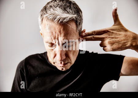 Portrait of mature man making shooting gesture with his hand against his temple Stock Photo