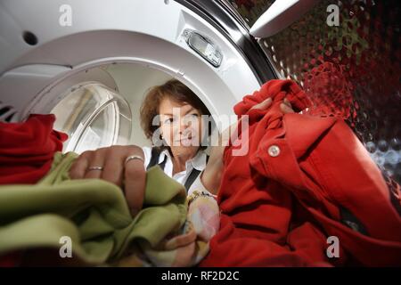 Housewife emptying a tumble dryer, removing the dry washing from the drum Stock Photo