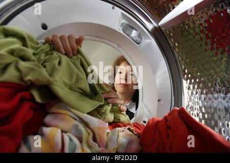 Housewife emptying a tumble dryer, removing the dry washing from the drum Stock Photo