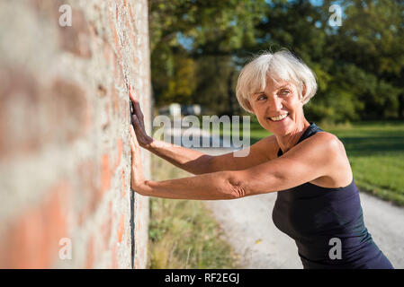 Smiling sportive senior woman leaning against a brick wall Stock Photo