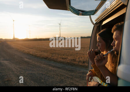 Couple brushing teeth in camper van in rural landscape at sunset Stock Photo