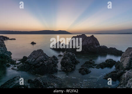 Long exposure photo of water going through rocks on the beautiful sunset, sun going behind island Stock Photo