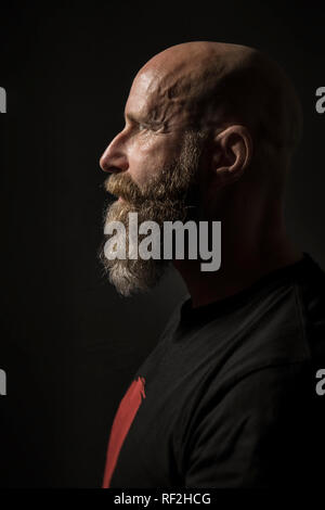 An image of a bearded man with a bald head side view and dark background Stock Photo