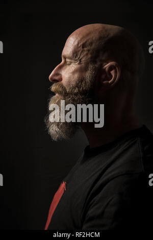 An image of a bearded man with closed eyes side view and dark background Stock Photo