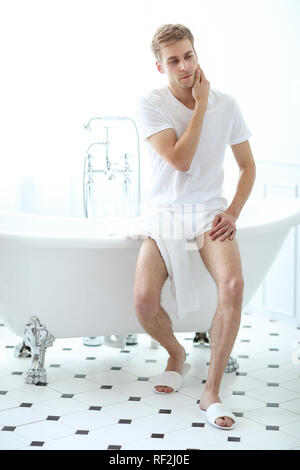 Handsome young man in bathtub at home having bath, washing body and