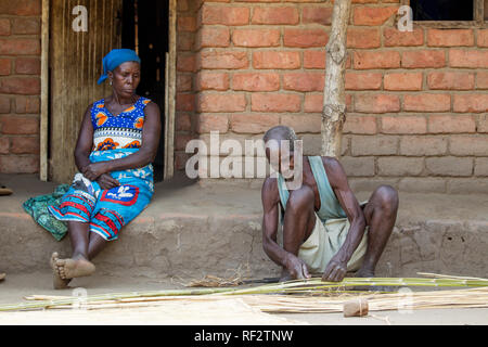 A Malawian man weaves a mat from reeds using traditional technique in a village in Chikwawa, Malawi as his wife looks on. Stock Photo