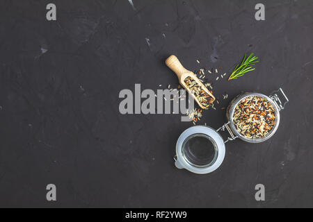 Black, purple, and white rice (Oryza sativa) mix in glass jar on black stone concrete textured surface background. Top view with copy space for your t Stock Photo