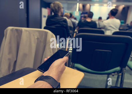 Detail of businessman hand holding a smart phone at conference. Stock Photo
