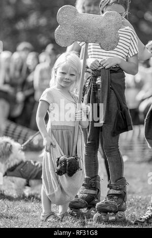 A little girl with her puppy in a sling holding a giant bone in the park at a dog show. Stock Photo