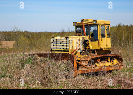 Old yellow rusty crawler tractor in the field. Old crawler tractor on overgrown field, Latvia. Stock Photo