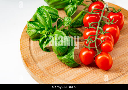 The branch of cherry tomatoes on a wooden background. Cherry tomatoes and basil leaves on a white background. Stock Photo