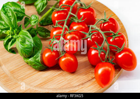 The branch of cherry tomatoes on a wooden background. Cherry tomatoes and basil leaves on a white background. Stock Photo