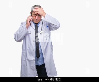 Handsome senior doctor man talking on smarpthone over isolated background stressed with hand on head, shocked with shame and surprise face, angry and  Stock Photo