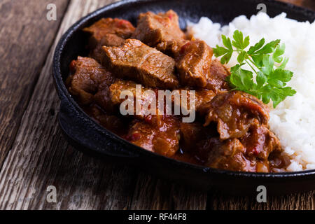 Beef stew served with white rice in cast iron skillet on rustic wooden table, close-up, selective focus Stock Photo