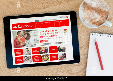 The Santander Bank website features on an iPad tablet device which rests on a wooden table beside a notepad (Editorial only). Stock Photo