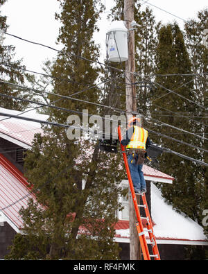 A man on a ladder working on fiber optic cable connections in Speculator, NY USA on a cold winter day. Stock Photo