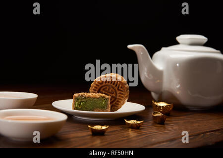 traditional delicious chinese mooncakes, tea pot and gold ingots on wooden table isolated on black Stock Photo