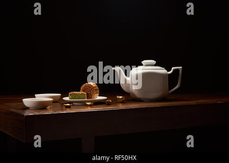traditional chinese mooncakes, tea pot and gold ingots on wooden table isolated on black with copy space Stock Photo