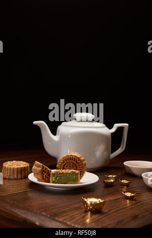 traditional chinese mooncakes, tea pot and gold ingots on wooden table isolated on black Stock Photo