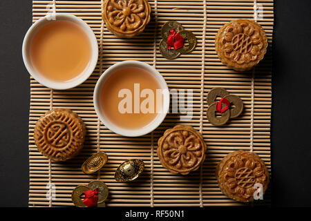 top view of mooncakes, feng shui coins and tea pot with cups on bamboo table mat Stock Photo