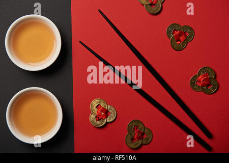 top view of tea cups, feng shui coins and chopsticks on red and black background Stock Photo