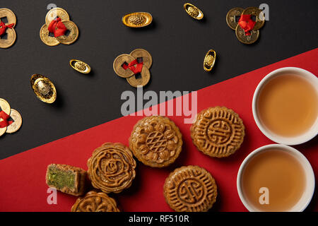 top view of mooncakes, feng shui coins and cups with tea on red and black background Stock Photo