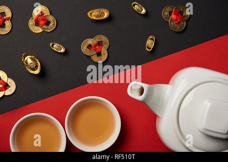 top view of tea pot, cups, gold ingots and feng shui coins on red and black background Stock Photo