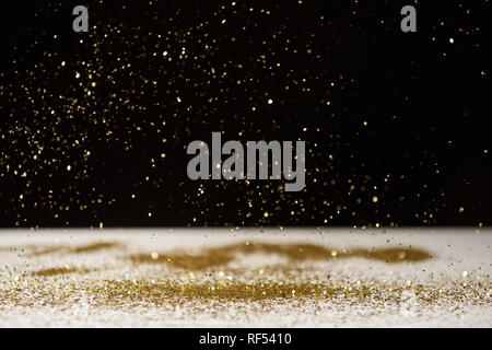 selective focus of bright sparkles falling on white table isolated on black Stock Photo