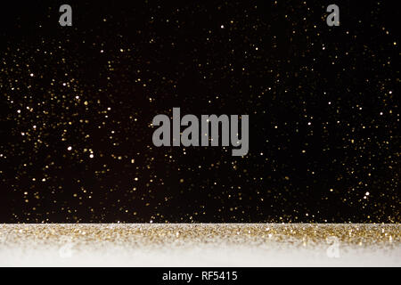 selective focus of golden sparkles falling on white table isolated on black Stock Photo