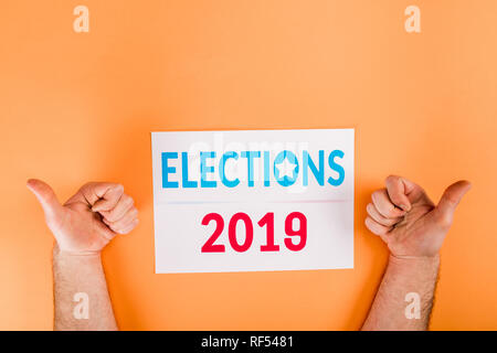 cropped view of man showing thumbs up near card with 'elections 2019' lettering isolated on orange Stock Photo