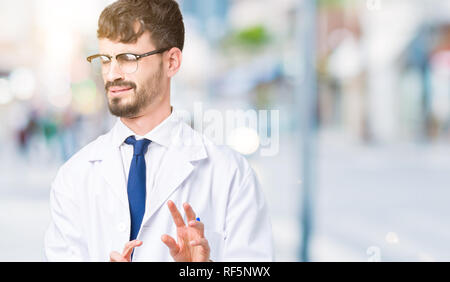 Young professional scientist man wearing white coat over isolated background disgusted expression, displeased and fearful doing disgust face because a Stock Photo
