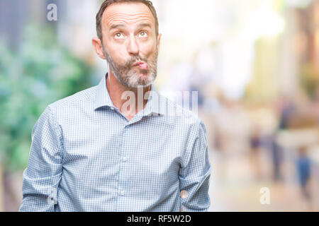 Middle age hoary senior business man over isolated background making fish face with lips, crazy and comical gesture. Funny expression. Stock Photo