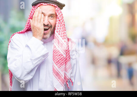 Senior arab man wearing keffiyeh over isolated background covering one eye with hand with confident smile on face and surprise emotion. Stock Photo