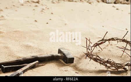 Religious Easter background with crown of thorns, a large old iron nail and small hammer on sand with copy space Stock Photo