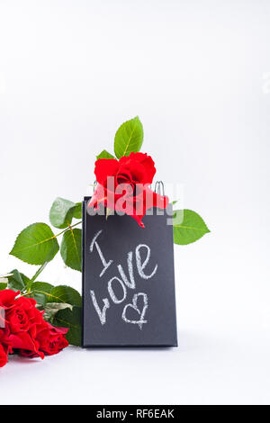 A bouquet of red roses and a letter with the text of love. Gift and flowers on a white background. The concept of lovers day and mother's Stock Photo