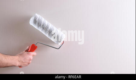 Hand with roller on white wall. Concept of painter and paint supplies. Horizontal composition. Stock Photo