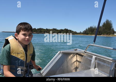Young boy in a life jacket, driving a small tinny boat on the Brunswick River, New South Wales, Australia Stock Photo