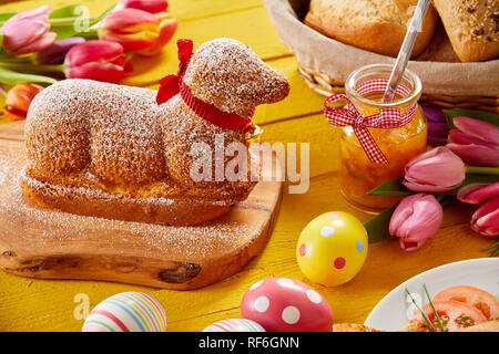 Gourmet lamb shaped Easter cake with colorful eggs and tulips on a festive table Stock Photo