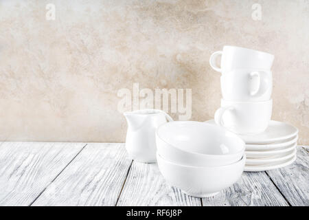 Assortment stack clean empty new white kitchen utensils, plates, bowls, cups mugs. On a white concrete background Stock Photo