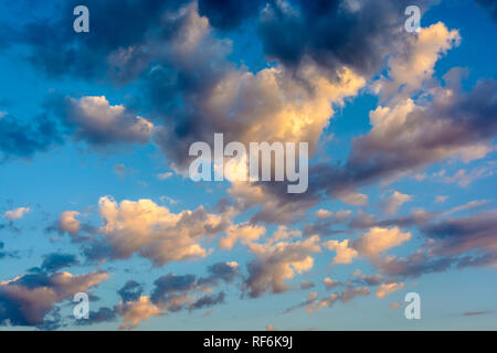 Cloudscape with dark and light, medium size clouds illuminated by the warm light of the setting sun against blue sky. Stock Photo