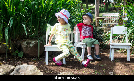 A photo of a boy and girl sitting together on white chair in a garden Stock Photo