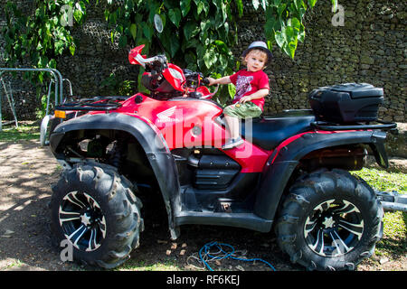 A photo of a 2 year old toddler sitting on a red Honda ATV, San Jose, Costa Rica Stock Photo