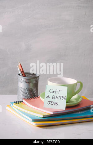 Green cup, notebooks and sticker with text - get a better job on light background. Toned business concept with copy space Stock Photo