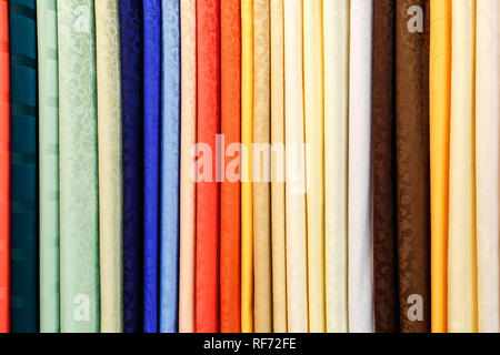 wide selection of different color textile silk fabrics clothes lay in row in drapery store Stock Photo