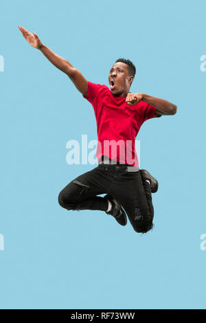 Forward motion. The happy surprised young african man jumping against blue studio background. Runnin man in motion or movement. Human emotions and facial expressions Stock Photo