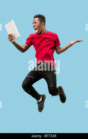 Image of happy excited young african man jumping isolated over yellow background using laptop computer. Stock Photo