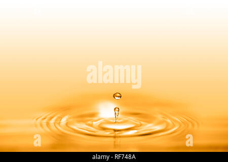 Closeup on drop of cosmetic golden oil liquid creating a circular wave. Stock Photo